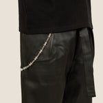 ICED London: close-up of black leather trousers with a silver chain hanging from the waist, paired with a black top.
