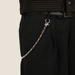 Black trousers with a ICED London silver chain attached to the belt loop, close-up detail.