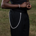 ICED London: person in black outfit with a silver chain belt draped from the waist, hands clasped, outdoors grassy field.