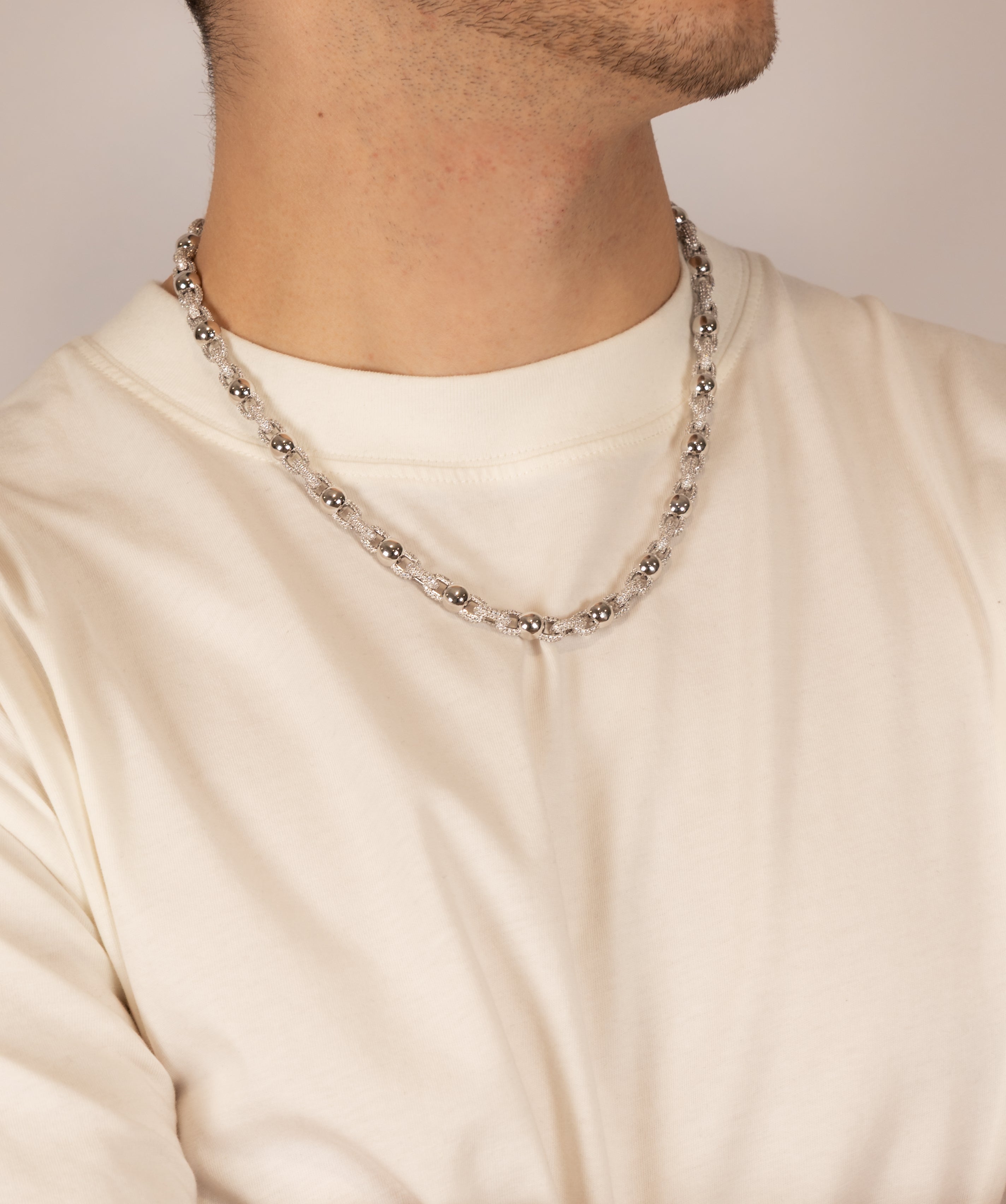ICED London silver bead chain necklace on a man’s white crew-neck T-shirt, close-up of neck and chin.